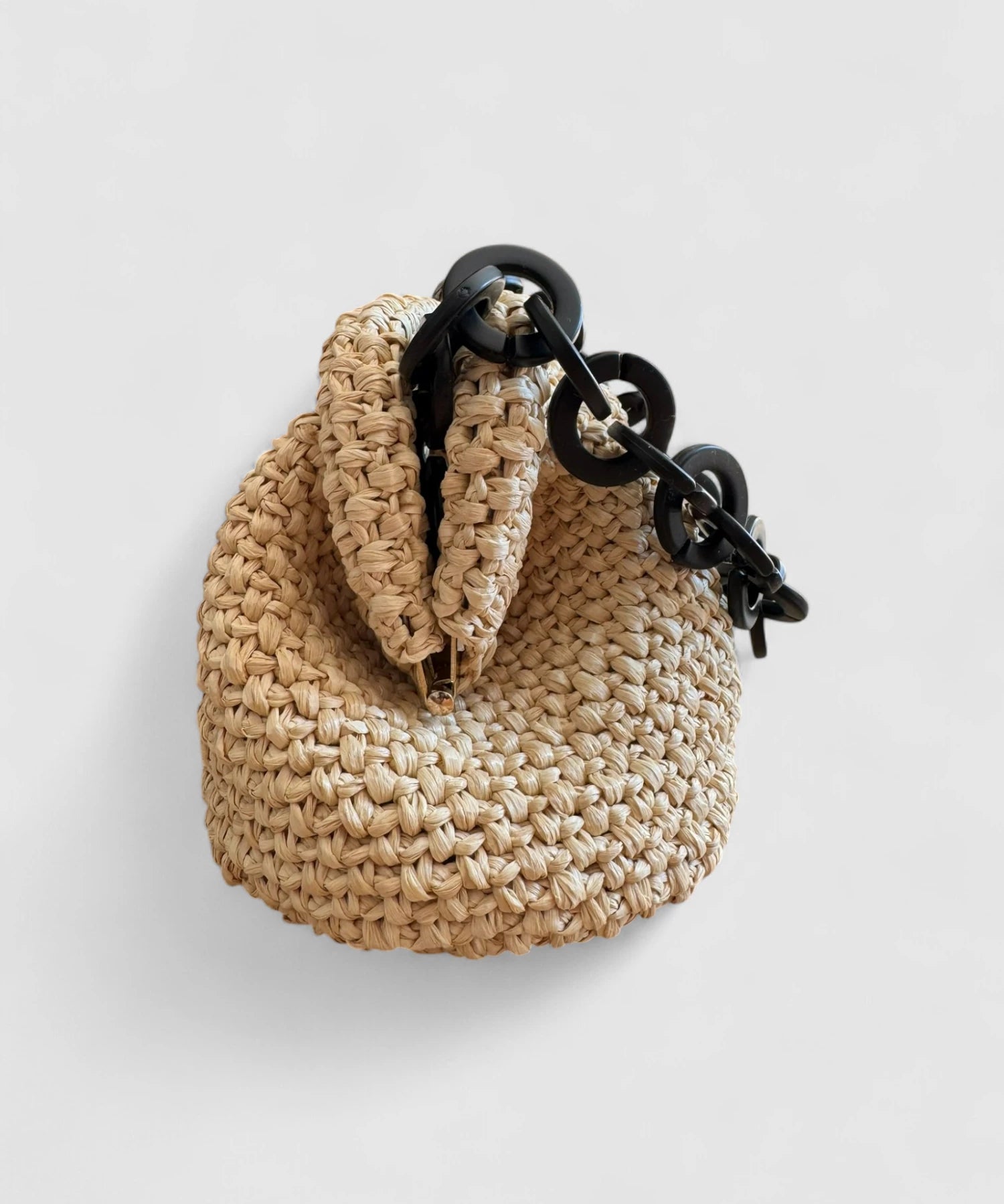 Vista lateral del clutch de rafia natural con detalle de cadena negra
