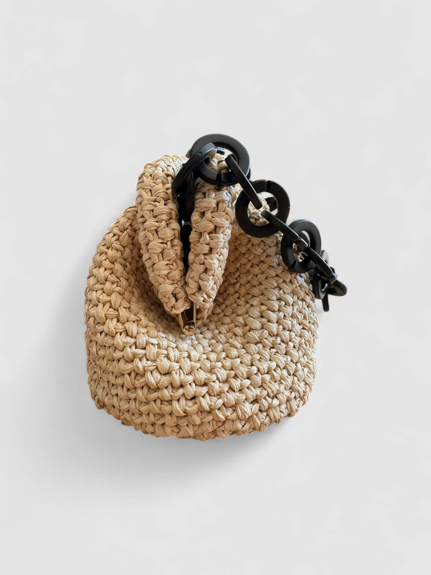 Vista lateral del clutch de rafia natural con detalle de cadena negra