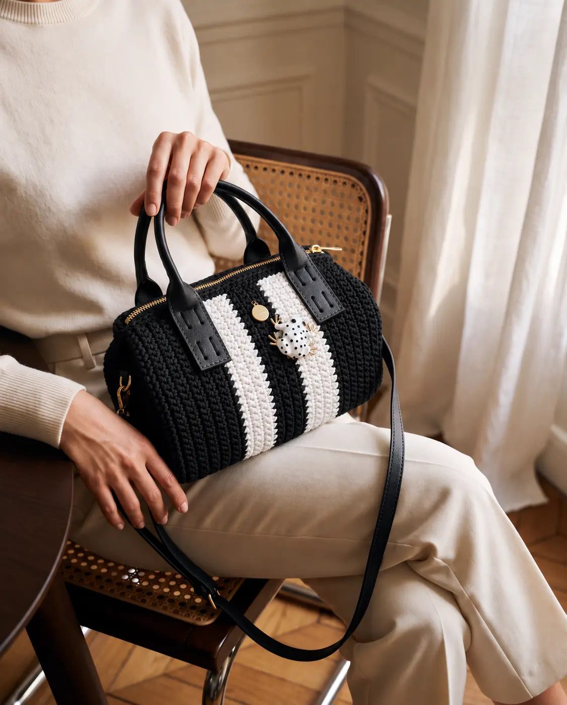 Modelo sentada con bolso Bowling Urbana Negro y Blanco tejido a mano sobre el regazo en un apartamento de inspiración parisina