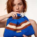 Close-up of Clutch Urbana Blue by The Labbo, with terracotta and ecru stripes and an enamelled frog, held by a model.