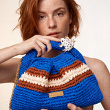 Close-up of Clutch Urbana Blue by The Labbo, with terracotta and ecru stripes and an enamelled frog, held by a model.