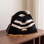 Clutch Urbana Black and White by The Labbo, with a gold chain and enamelled frog, on a wooden console beside a curtain.