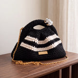 Clutch Urbana Black and White by The Labbo, with a gold chain and enamelled frog, on a wooden console beside a curtain.