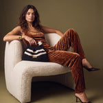 Model in a copper-coloured velvet outfit, seated in a light armchair and holding Clutch Urbana Black and White by The Labbo.