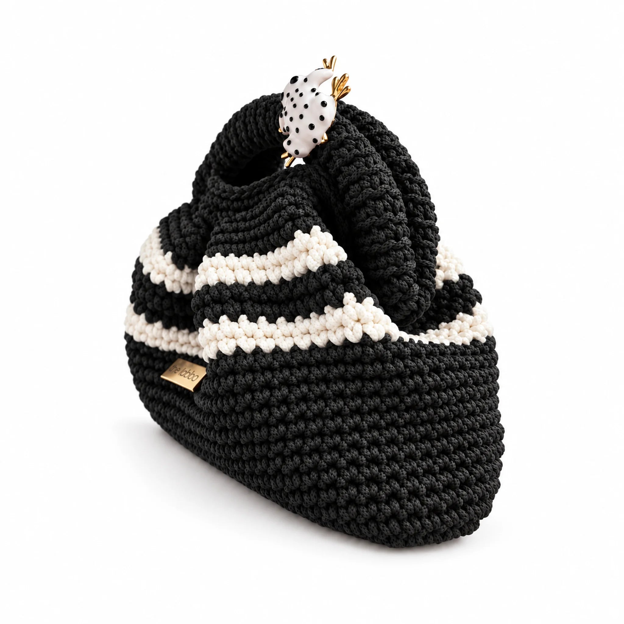 Three-quarter view of Clutch Urbana Black and White by The Labbo, showing the folds, stripes and yarn-covered handle in black and white.