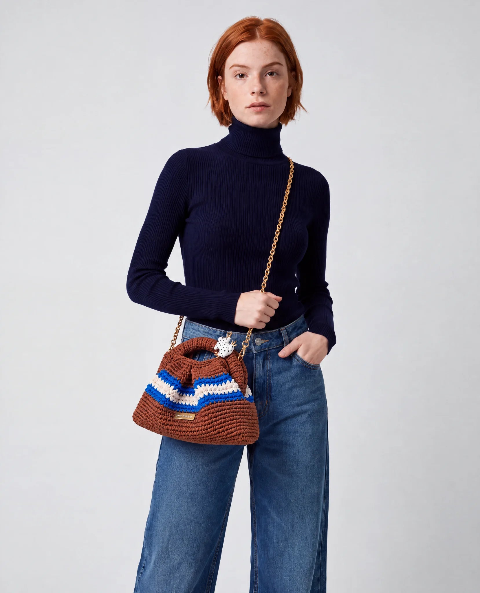 Modelo con jersey azul marino y vaqueros llevando el Clutch Urbana Terracota de The Labbo con su cadena dorada.