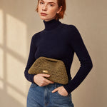 Clutch dorado envejecido de crochet The Labbo, llevado en la mano con jersey azul marino y vaqueros.