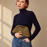 Clutch dorado envejecido de crochet The Labbo, llevado en la mano con jersey azul marino y vaqueros.
