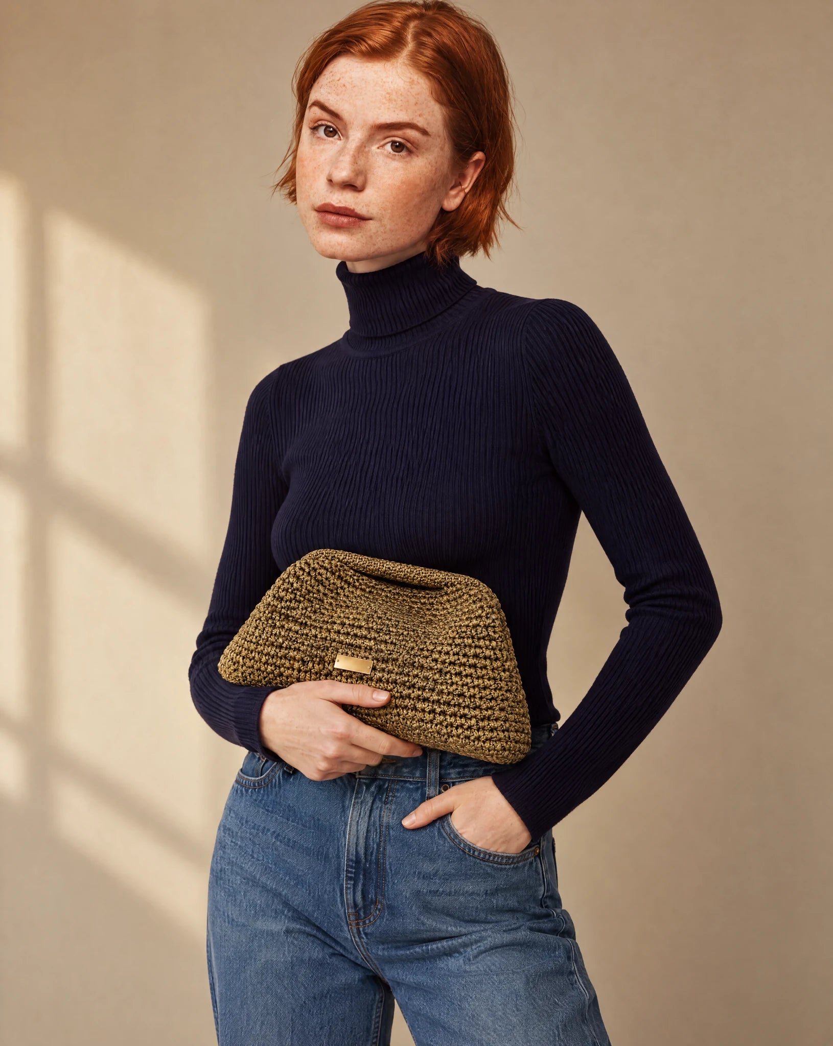 Clutch dorado envejecido de crochet The Labbo, llevado en la mano con jersey azul marino y vaqueros.